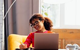 Smiling young African woman is writing in notebook at...