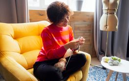 Young African smiles and knits at home in living room....