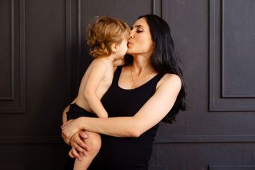 An attractive pregnant woman in a black dress kisses her...