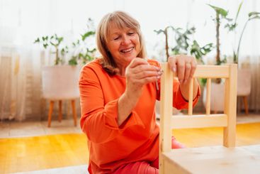 Elderly woman in orange casual clothes assembles wooden...