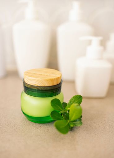 A close-up of a jar of green glass cream with a wooden...