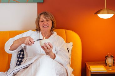 An elderly woman in a white bathrobe lies in bed and...