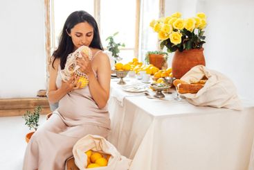 Young pregnant woman is sitting in kitchen and holding...