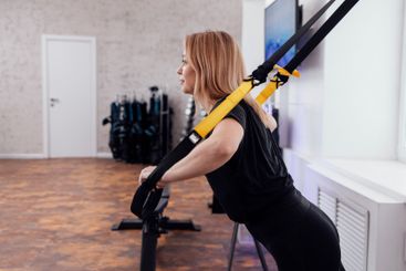 Beautiful sportswoman in black sportswear uses trx...