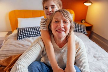 An elderly woman and her granddaughter hug and sit on...