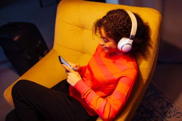 Smiling African woman is sitting in armchair and using...