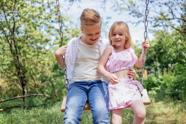 Blond boy and girl laugh and swing on swing. Joyful kids...