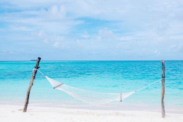 An empty hammock on the ocean coast. A clean white beach...
