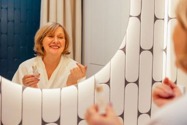 An elderly woman in a white terry dressing gown applies...