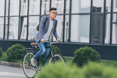 stylish asian man in gray jacket biking in city