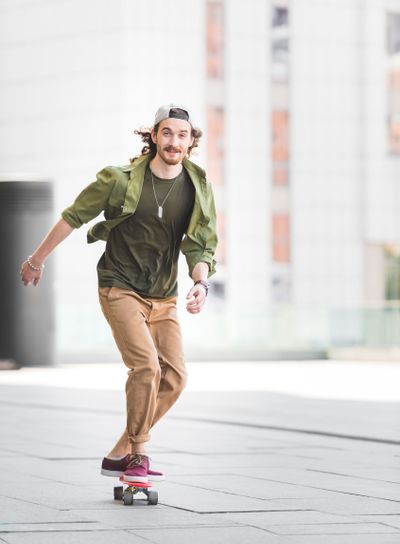 happy man looking at camera, riding on skateboard in city