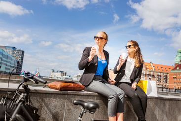 Two women sitting on wall and drinking coffee