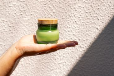 Close-up of a female hand with a jar of green frosted...