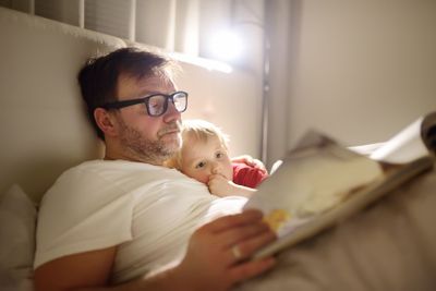Father reading bedtime stories to child. Dad putting son...
