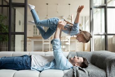 Relaxed young man raising in air carefree child daughter.
