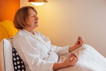 An elderly woman in a white coat is sitting in bed and...