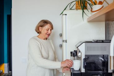 An elderly woman in a sweater is making coffee in the...